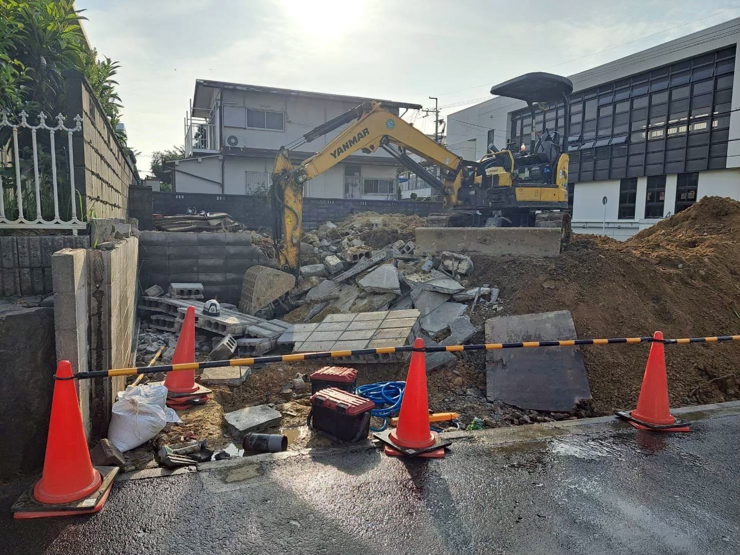 重機2台でブロック塀と基礎を解体している現場。道路側はカラーコーンで区切っている
